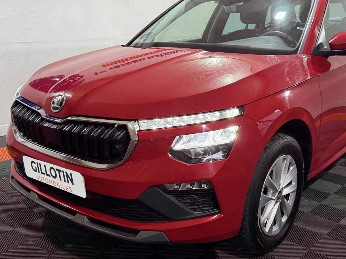 Vue 3/4 avant droite d'un Skoda Kamiq rouge 2024 avec calandre noire et phares LED allumés.