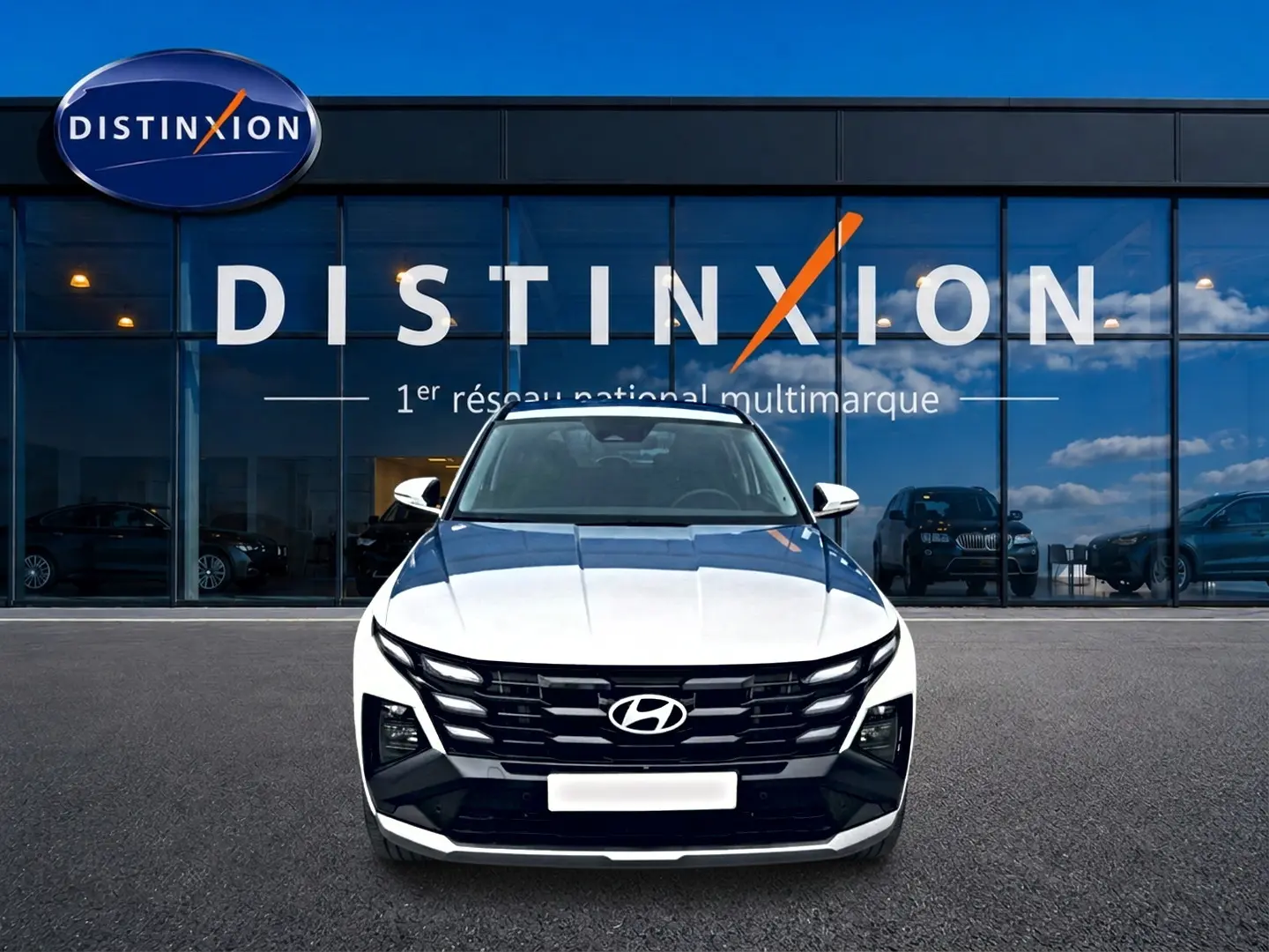 Vue avant d'un Hyundai Tucson blanc 2026 garé devant une vitrine avec logo Distinxion en arrière-plan.