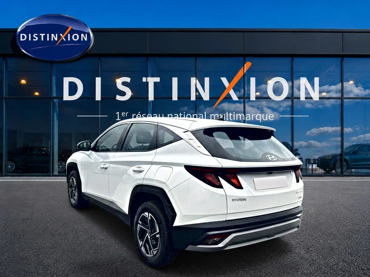 Vue 3/4 arrière droite d’un Hyundai Tucson blanc 2026 devant une vitrine avec logo Distinxion.