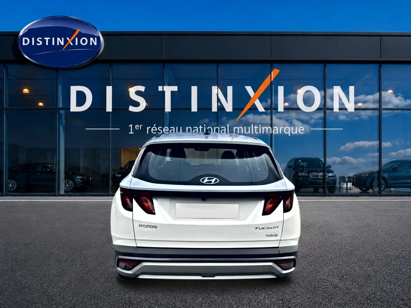Vue arrière d'un Hyundai Tucson blanc hybride 2026 garé devant une vitrine avec logo Distinxion.