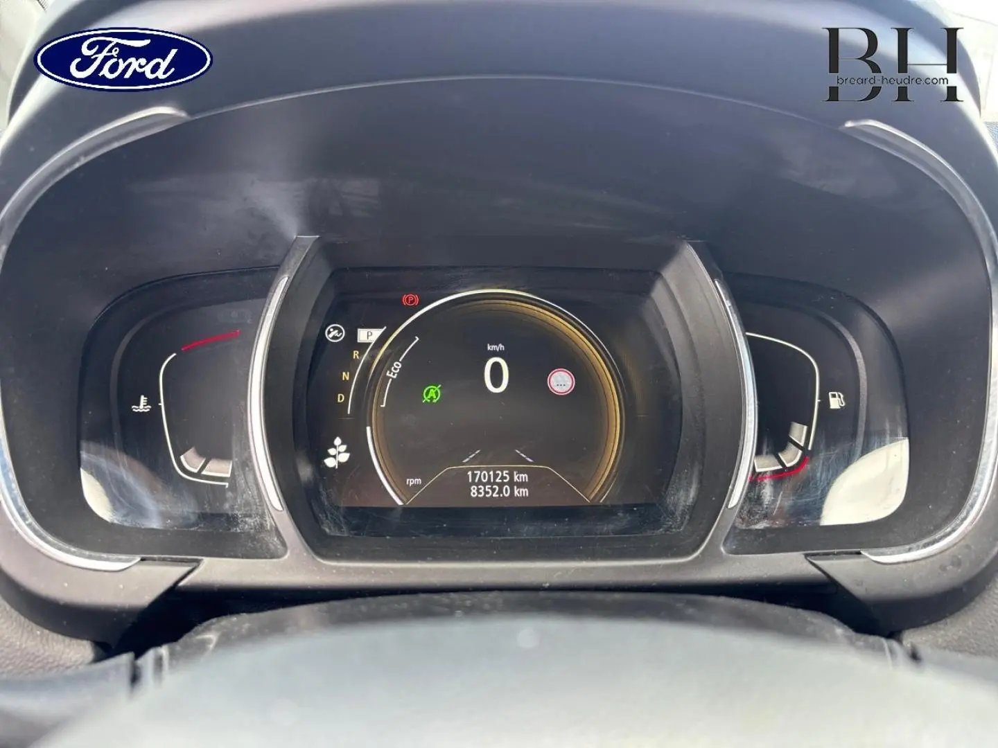 Vue rapprochée du tableau de bord numérique d'un Renault Grand Scenic gris, affichant 0 km/h et 170125 km au compteur.