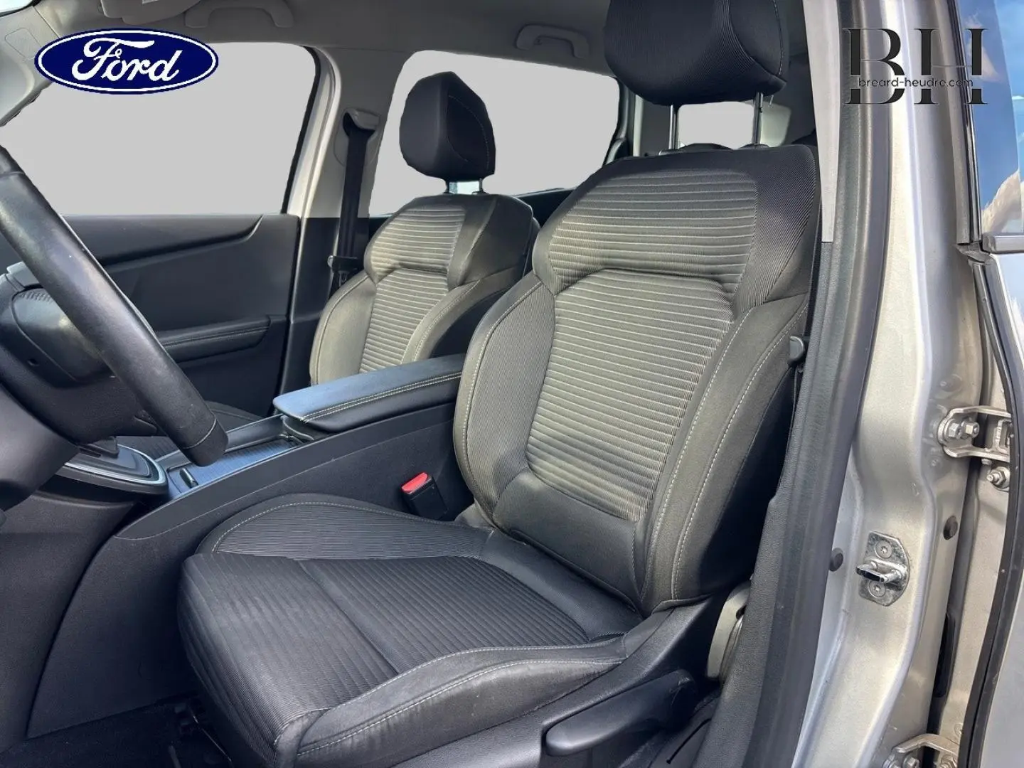 Vue intérieure côté conducteur du Renault Grand Scenic gris platine, mettant en valeur les sièges tissu carbone foncé embossé et l'accoudoir central.