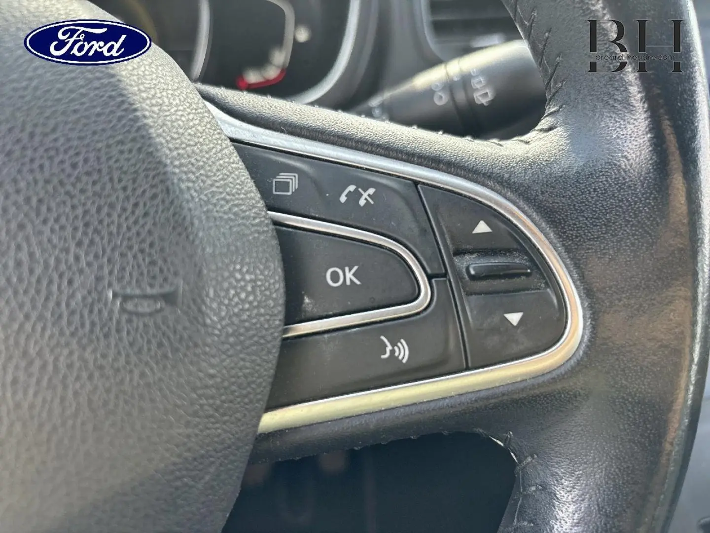 Gros plan sur les commandes au volant en cuir noir d’un véhicule, avec boutons multifonctions visibles.