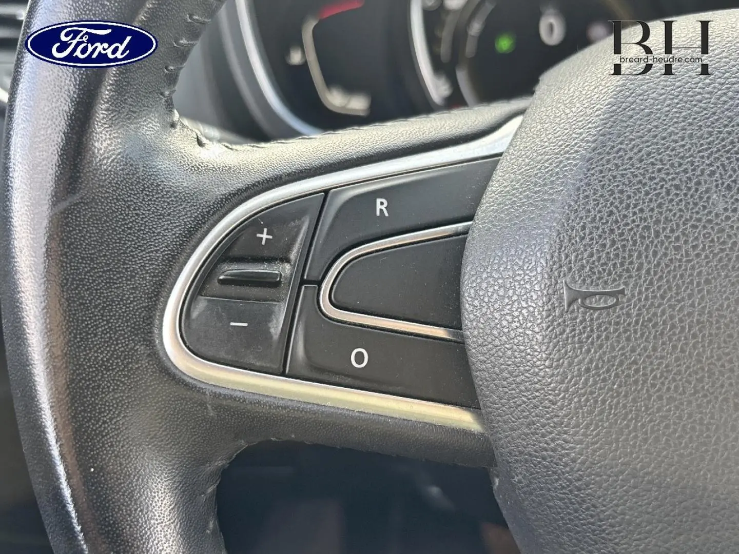 Gros plan sur les commandes du volant en cuir noir d’un véhicule, avec boutons de réglage du régulateur de vitesse.