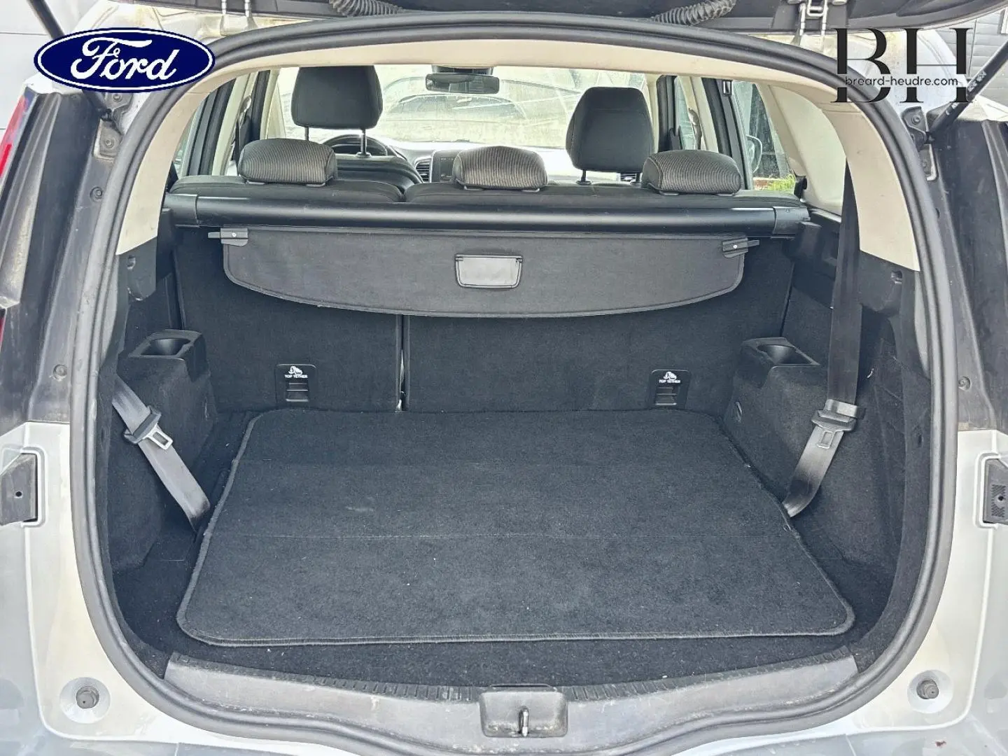 Coffre ouvert vu de l'arrière d'un Renault Grand Scenic gris platine avec cache-bagages et sièges arrière visibles.