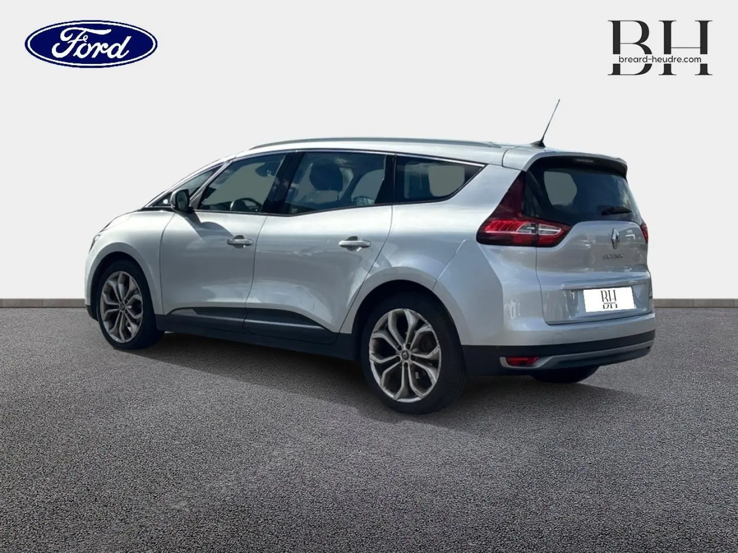 Vue 3/4 arrière droite d'un Renault Grand Scenic gris platine avec vitres teintées et barres de toit visibles.