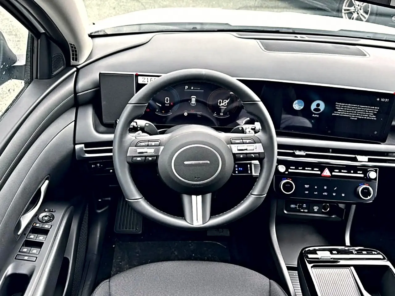 Vue intérieure frontale du tableau de bord du Hyundai Tucson 2026, volant cuir multifonction et écran digital large.