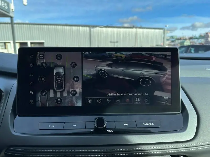 Écran central affichant la vue 360° et 3/4 arrière du Nissan Qashqai Hybrid e-POWER gris Argile 2025 en stationnement.