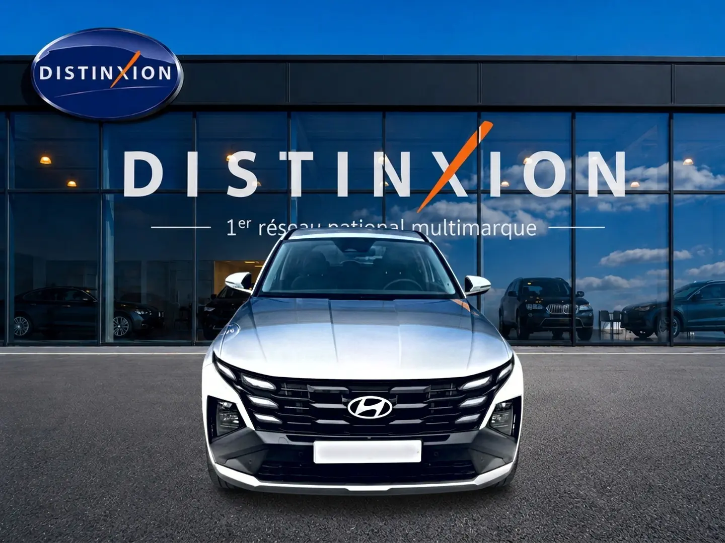 Vue avant du Hyundai Tucson blanc 2026 devant une vitrine avec logo Distinxion, mettant en valeur sa calandre noire distinctive.
