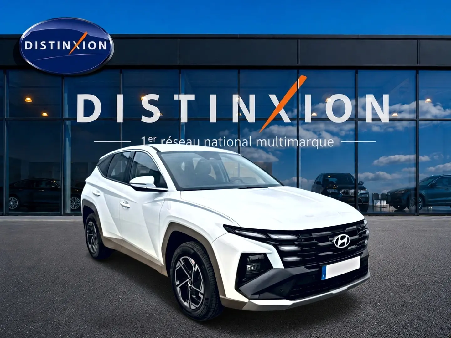 Hyundai Tucson blanc en 3/4 avant droit, avec calandre noire et jantes alliage 17 pouces devant vitrine Distinxion.