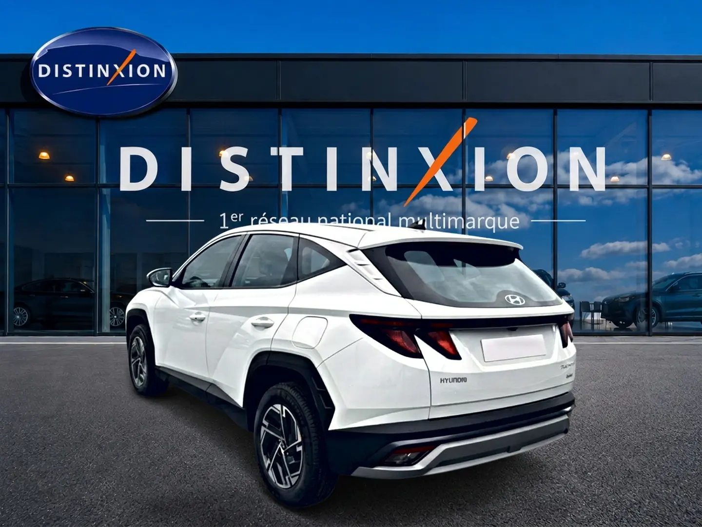 Vue 3/4 arrière gauche du Hyundai Tucson blanc 2026 avec jantes alliage et feux arrière LED, devant une vitrine Distinxion.