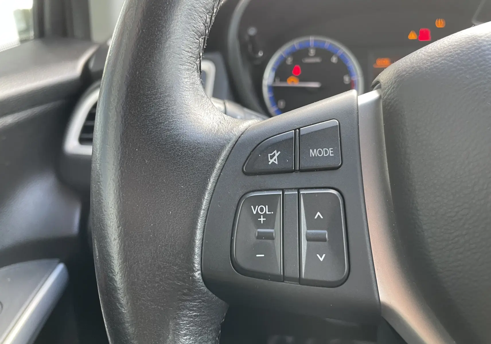 Gros plan sur les commandes au volant du Suzuki SX4 S-CROSS 2016, boutons de volume et mode audio visibles.