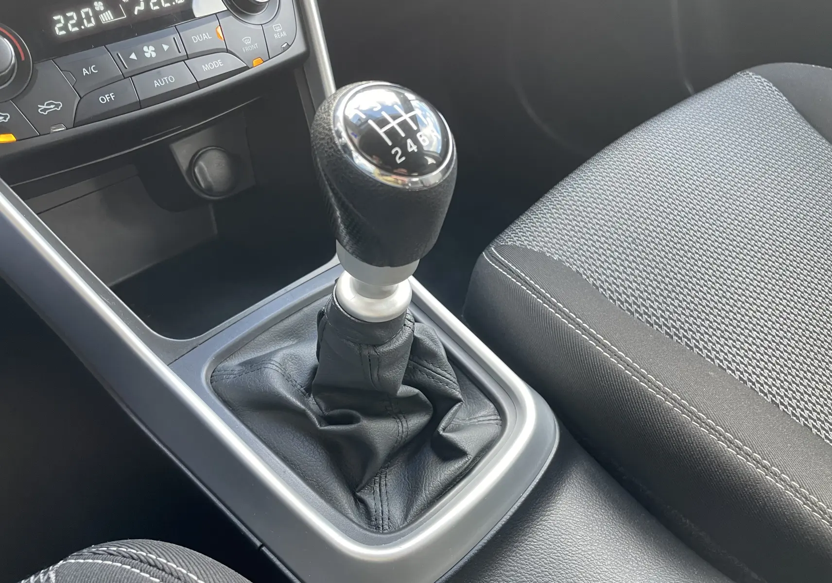 Le levier de vitesses manuel noir et argenté du Suzuki SX4 S-CROSS 2016, avec partie avant de la console et siège tissu gris.