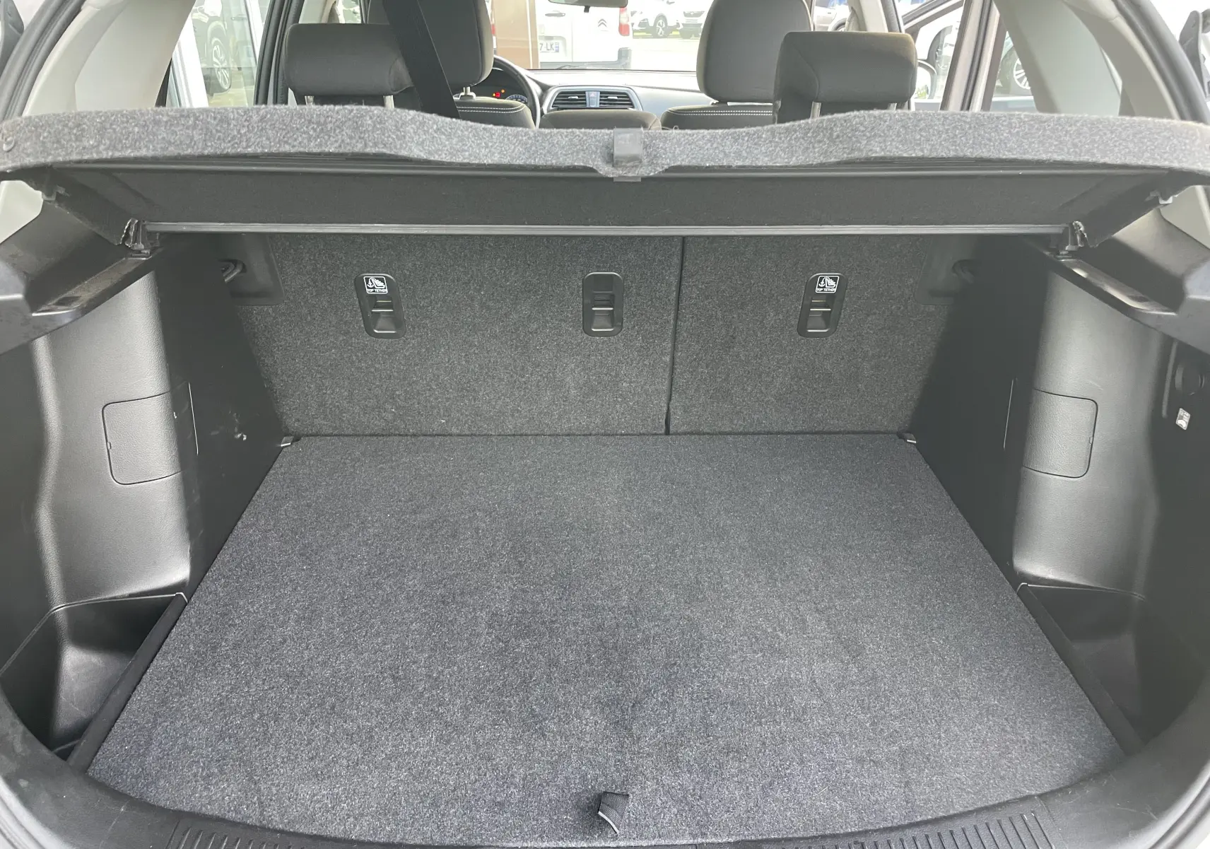 Coffre ouvert d'un Suzuki SX4 S-CROSS gris, montrant l'espace de chargement et la banquette arrière rabattable.