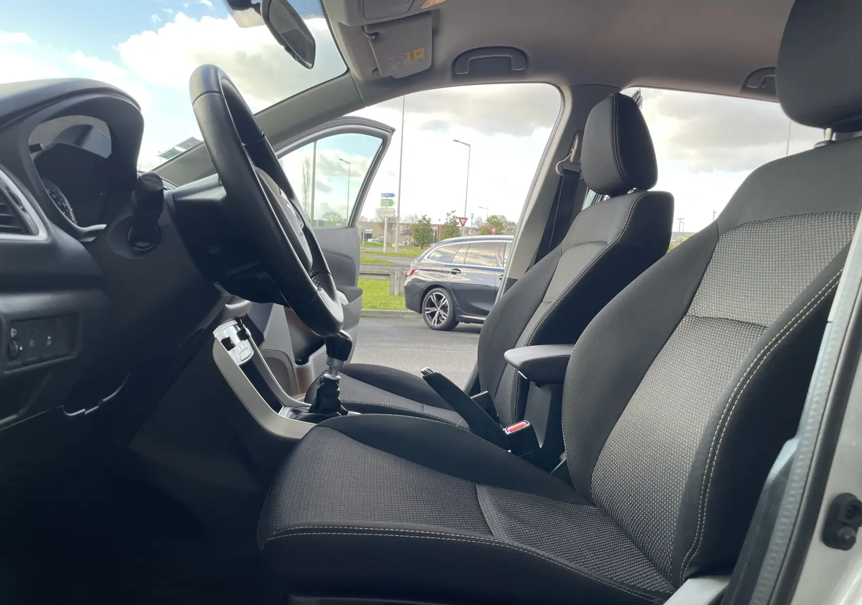 Intérieur du Suzuki SX4 S-Cross 2016 vu côté conducteur, sièges noirs en tissu et volant avec levier de vitesse manuel.