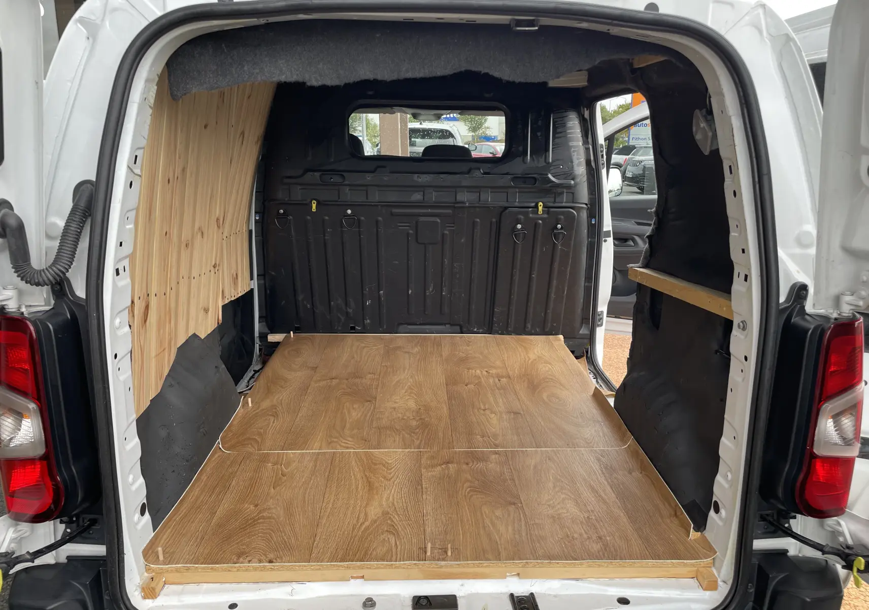 Vue arrière ouverte du Citroën Berlingo blanc 2018 avec aménagement intérieur en bois clair sur le plancher et côté gauche.