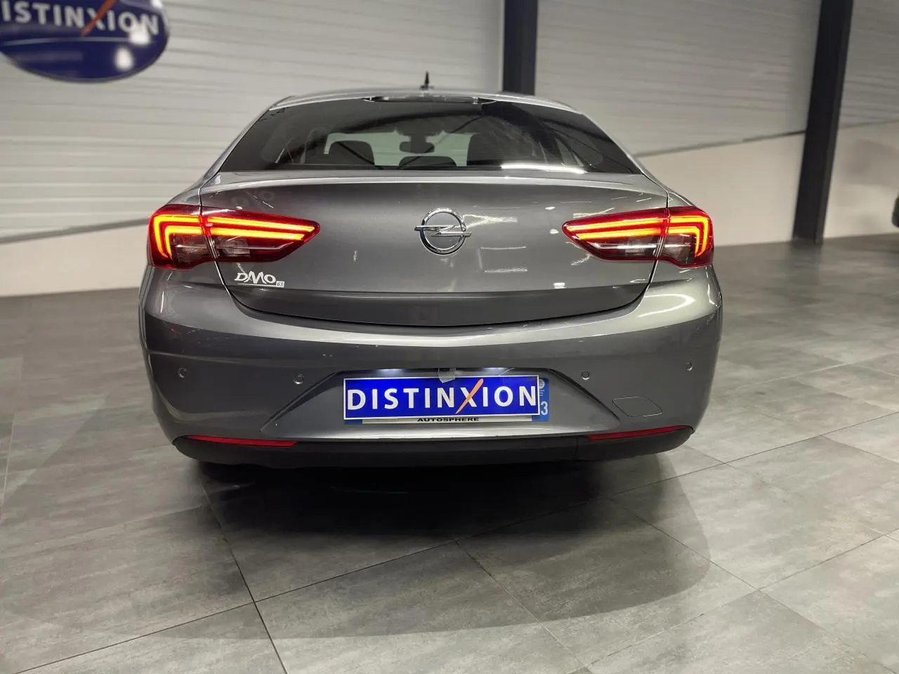 Vue arrière d'une Opel Insignia Grand Sport gris clair avec feux arrière LED allumés dans un showroom.
