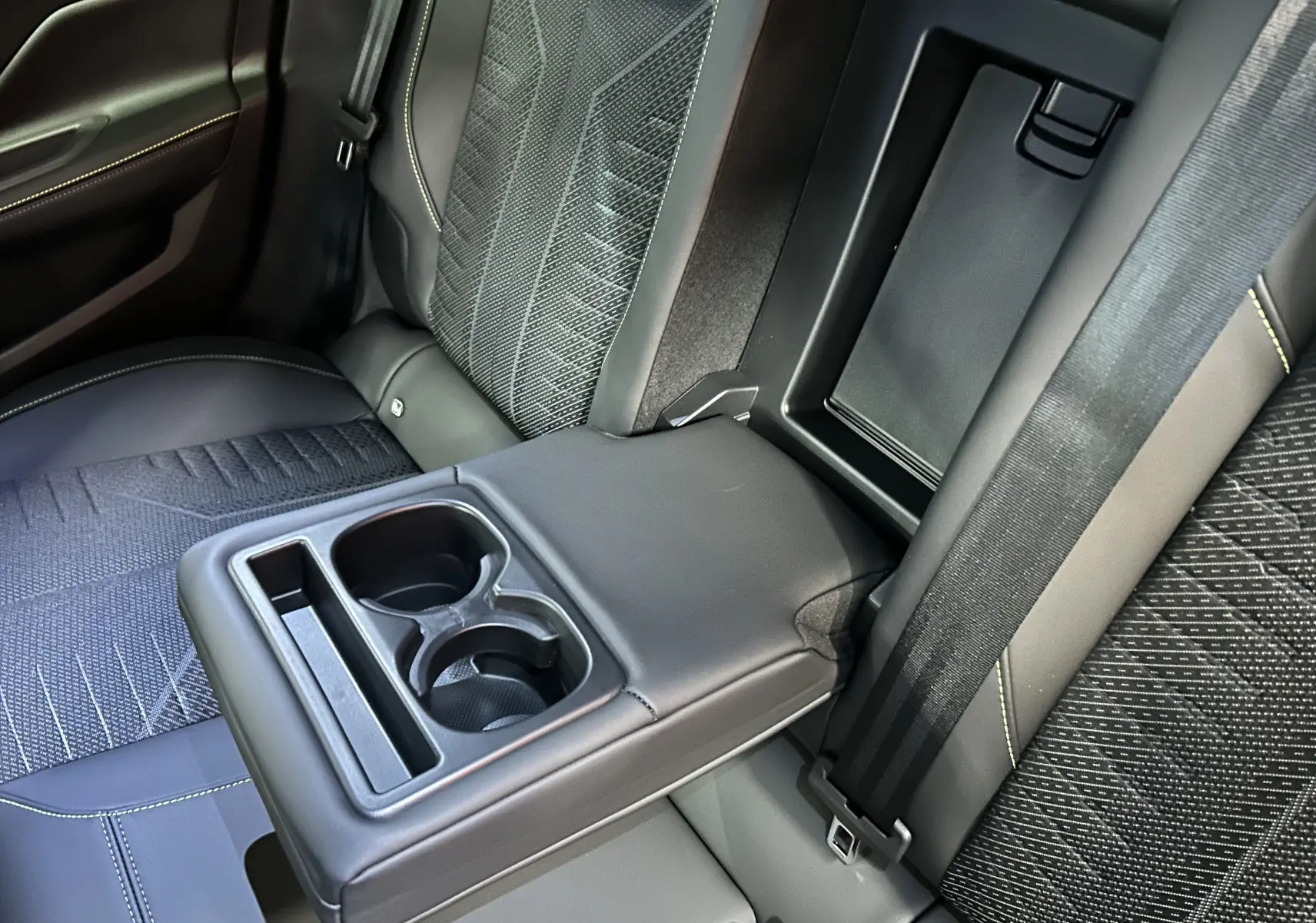 Gros plan sur l'accoudoir arrière rabattable avec porte-gobelets, sièges gris Artense à surpiqûres contrastées dans une Peugeot 308.