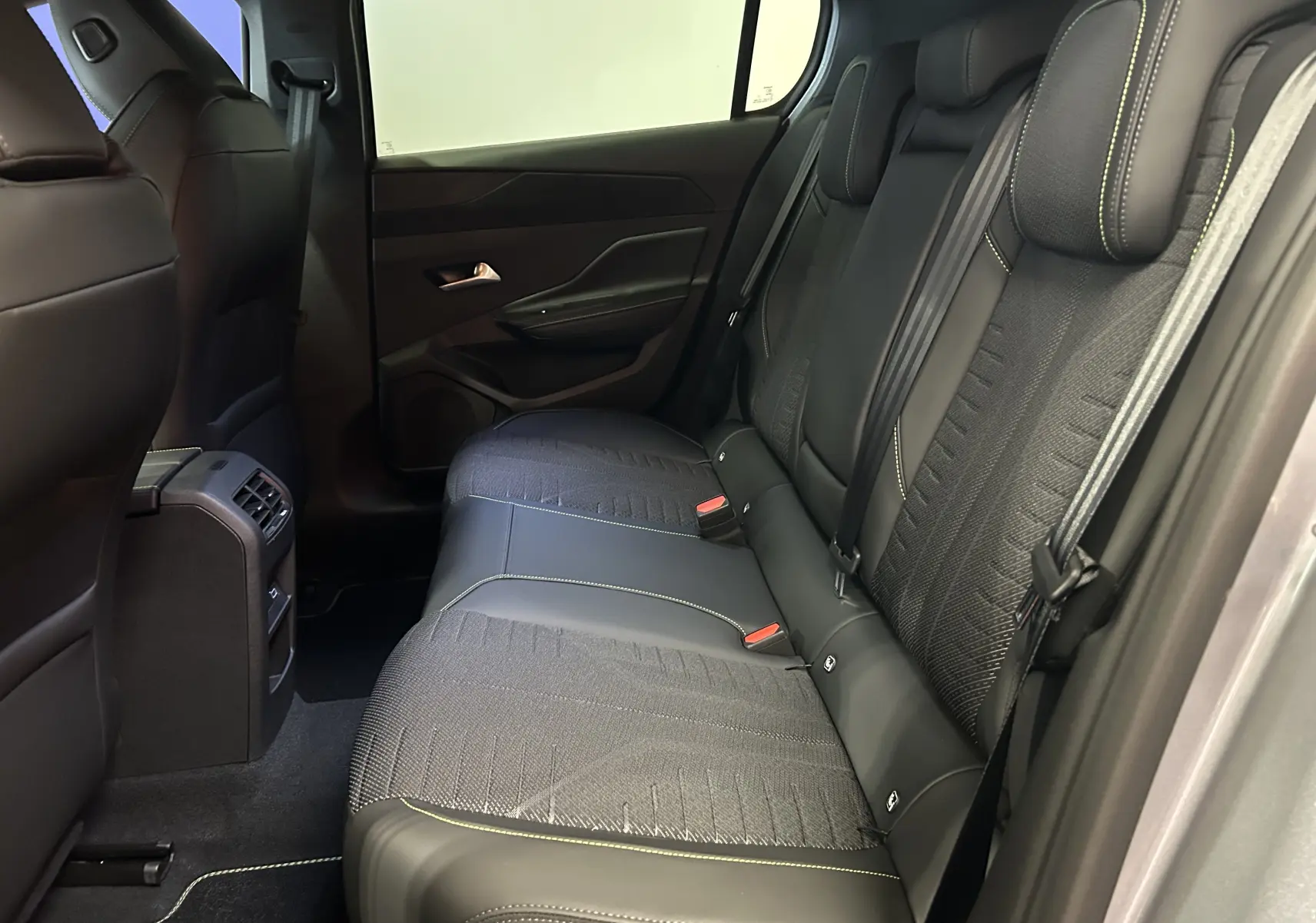Vue intérieure arrière côté droit de la Peugeot 308 III Ph.2 GT avec sièges tissu et cuir noirs à surpiqûres vertes.