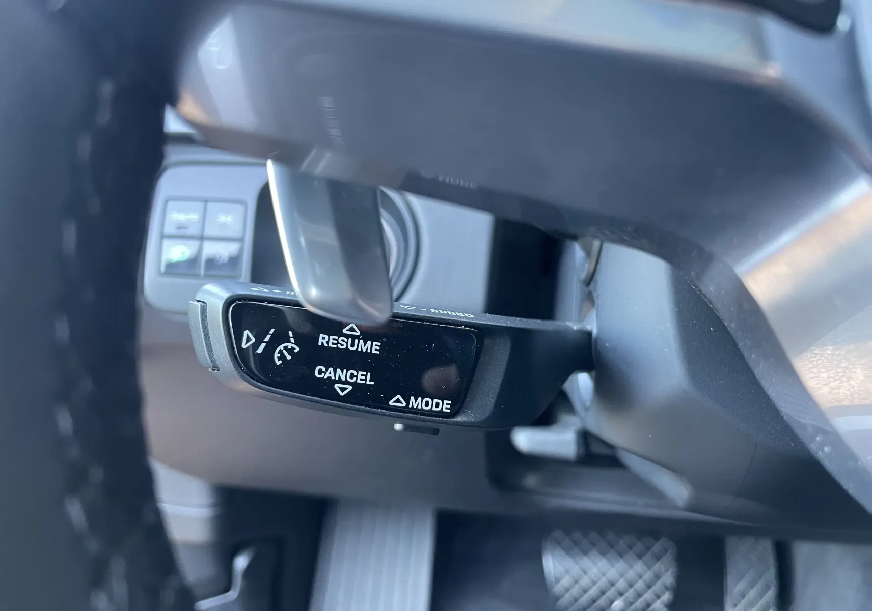 Gros plan sur la commande de régulateur de vitesse au volant d’un Porsche Cayenne Coupé E-Hybrid noir, intérieur gris/noir.