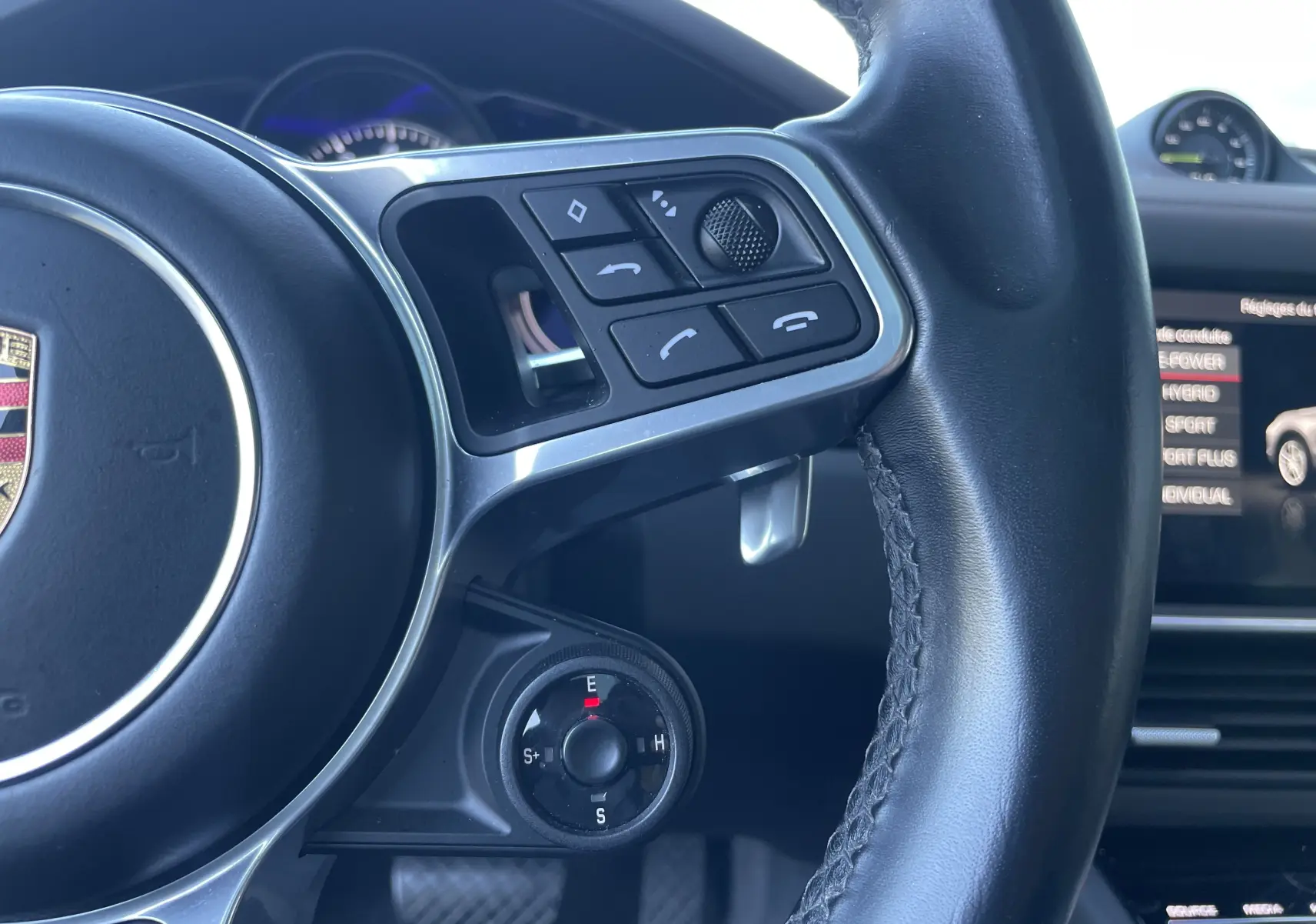 Gros plan sur le volant cuir noir du Porsche Cayenne Coupé e-Hybrid avec commandes multifonctions et sélecteur de mode de conduite.