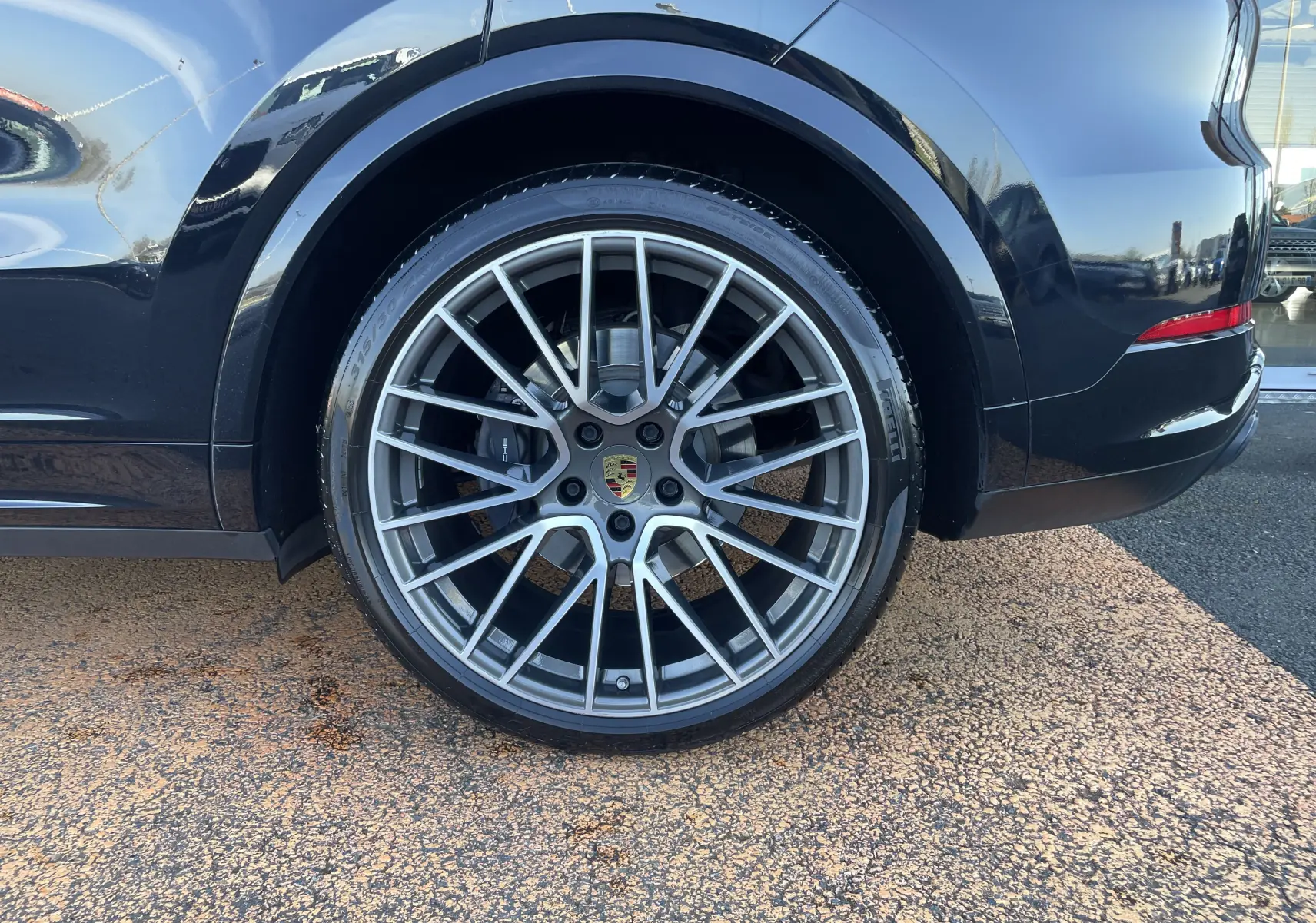 Gros plan sur la roue arrière droite du Porsche Cayenne Coupé E-Hybrid noir avec jante alu 22 pouces au design sportif.