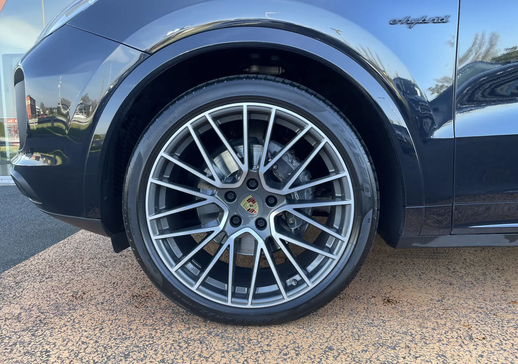 Gros plan sur la roue avant droite noire d’un Porsche Cayenne Coupé E-Hybrid avec jante alu 22 pouces et logo Porsche.