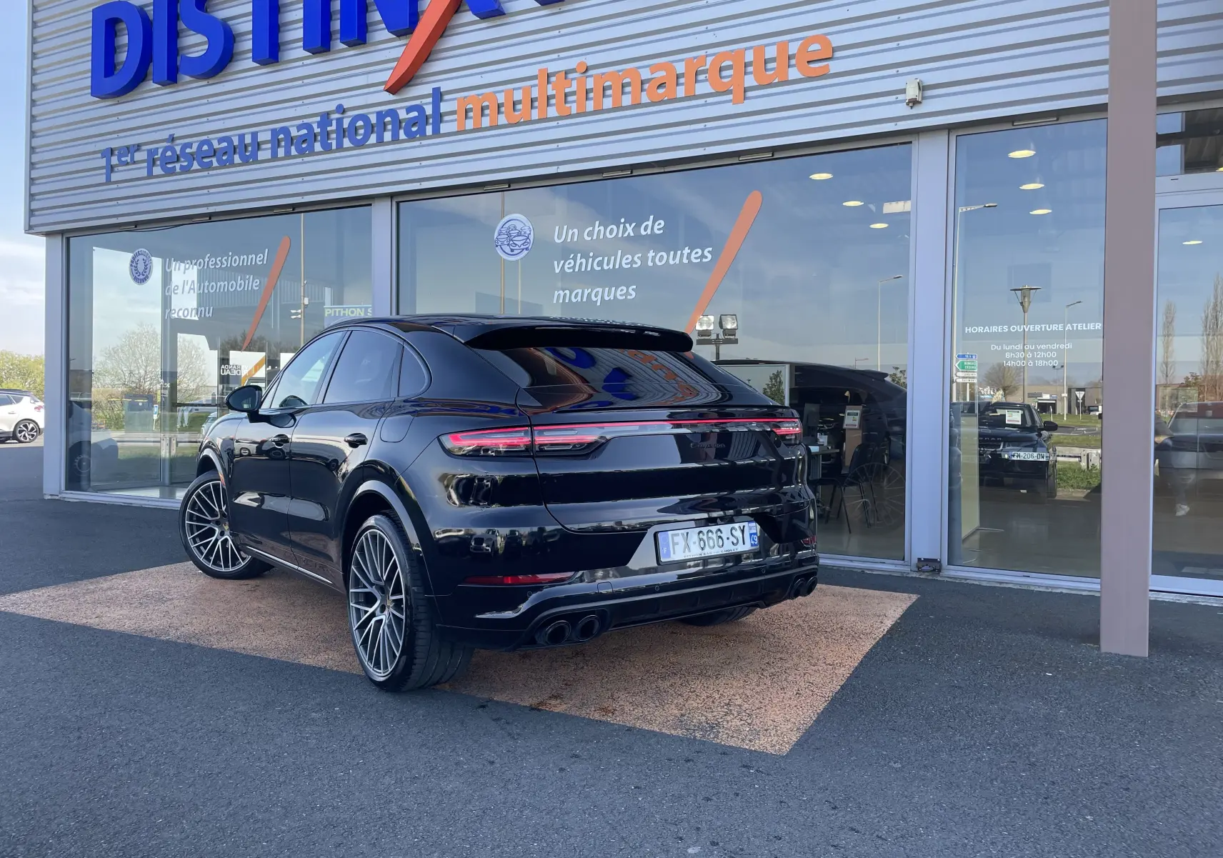 Vue 3/4 arrière droite d’un Porsche Cayenne Coupé E-Hybrid noir brillant avec jantes alu 22 pouces devant un showroom.
