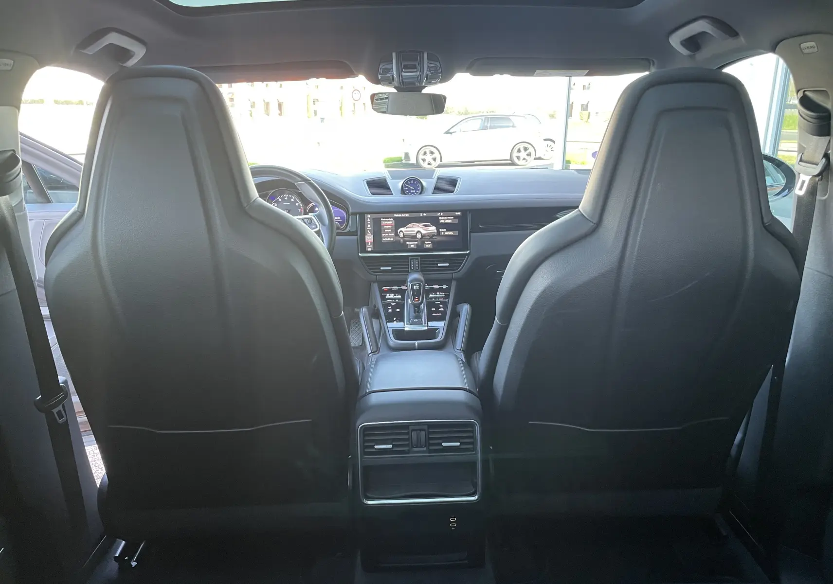 Vue intérieure arrière du Porsche Cayenne Coupé e-Hybrid noir, mettant en valeur les sièges sport en cuir et le toit panoramique.
