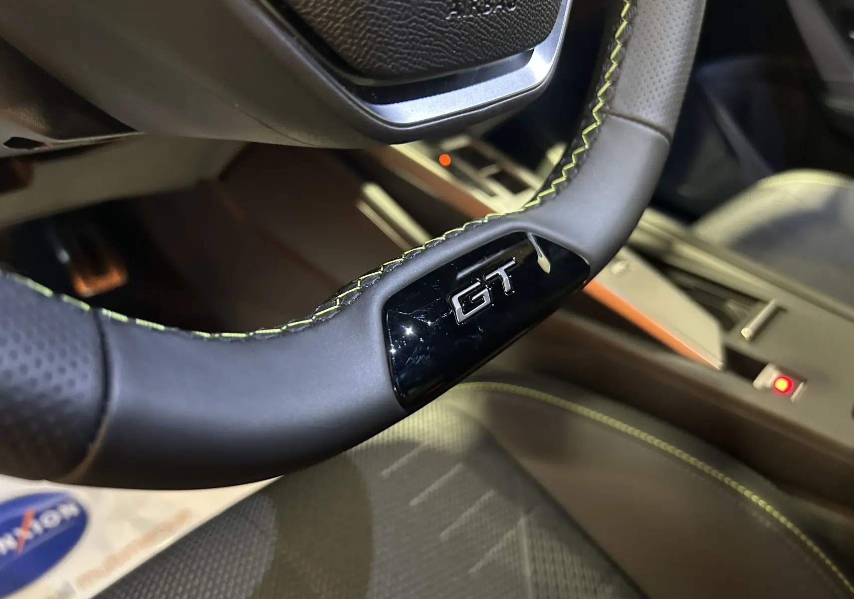 Gros plan sur le volant cuir noir avec surpiqûres vertes et logo GT de la Peugeot 308 Hybrid 2026.