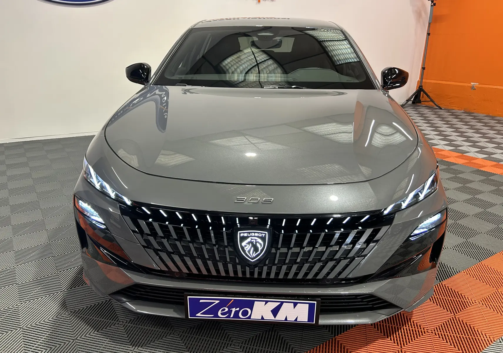 Vue avant frontale d'une Peugeot 308 III Ph.2 Hybrid 145 GT gris Selenium avec calandre noire et éclairage LED allumé.