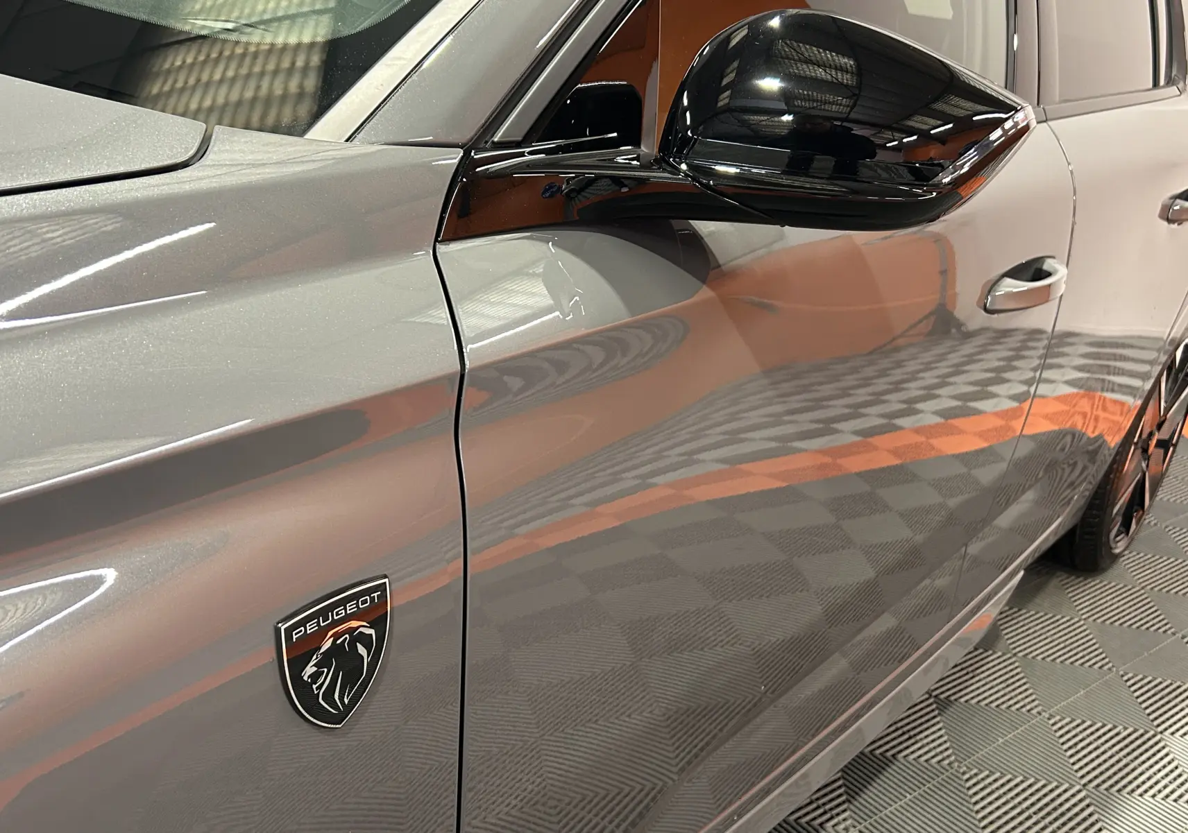 Gros plan sur la porte côté gauche d’une Peugeot 308 gris Selenium avec logo lion et rétroviseur noir brillant.