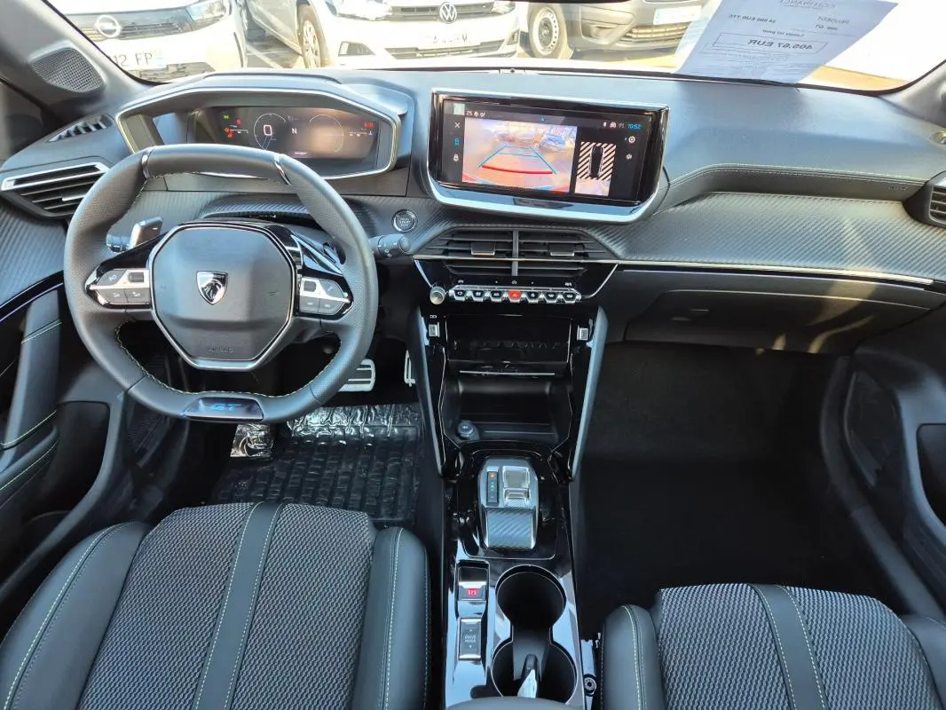 Vue intérieure frontale du poste de conduite de la Peugeot 208 Hybrid 136 GT avec volant compact et écran tactile central.