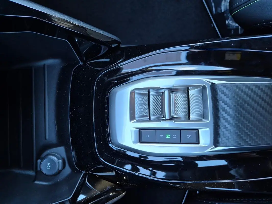Vue plongeante sur la console centrale noire de la Peugeot 208 Hybrid 136 e-DCS6 GT avec sélecteur de boîte auto et prise 12V.