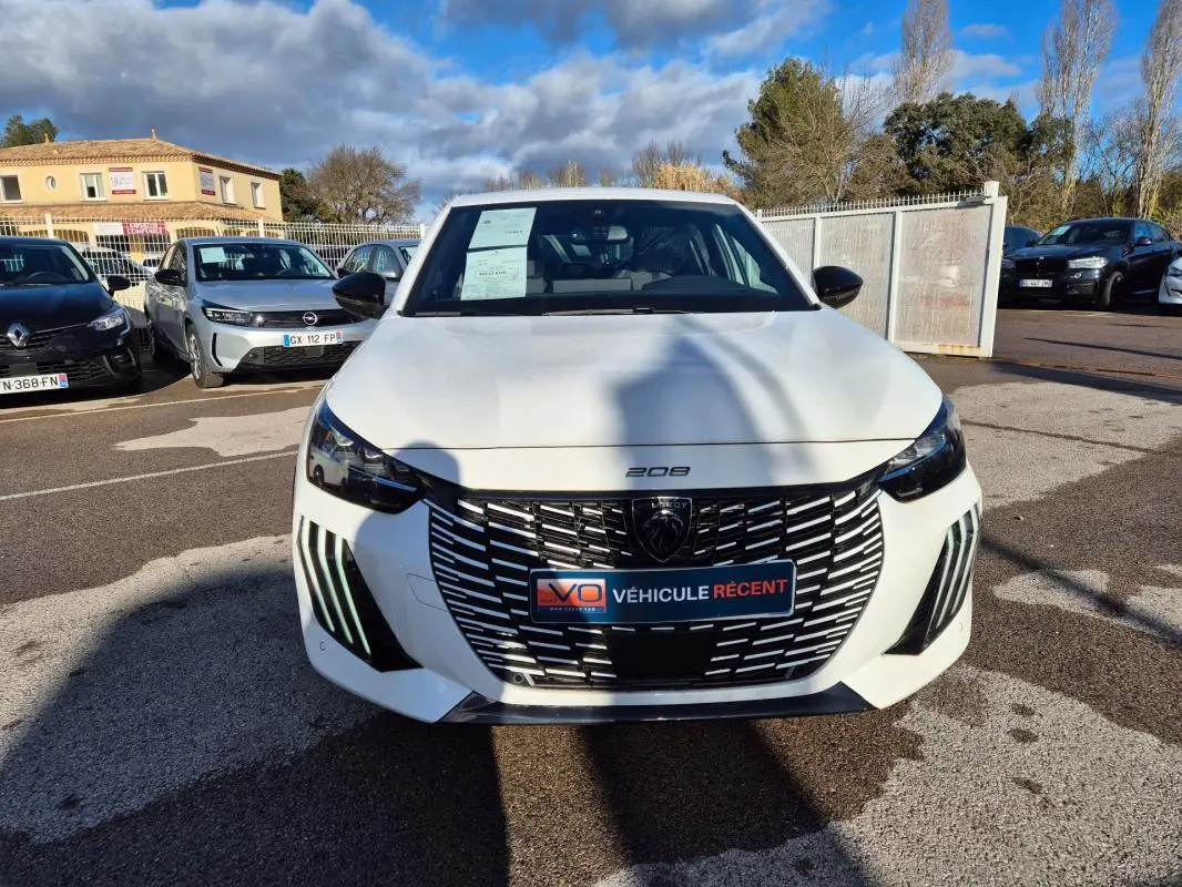 Vue de face d'une Peugeot 208 Hybrid 136 e-DCS6 GT blanche avec calandre noire et feux LED diurnes distinctifs.