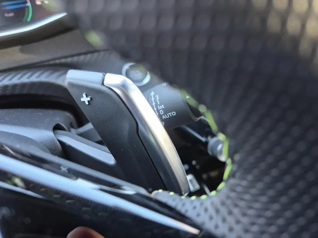 Gros plan sur la palette de changement de vitesse + au volant perforé d’une Peugeot 208 Hybrid 136 e-DCS6 GT.