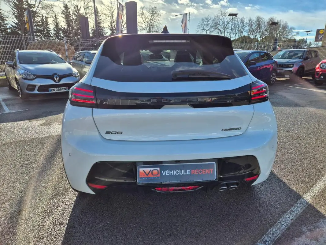 Vue arrière d'une Peugeot 208 Hybrid blanche de 2025, avec feux LED distinctifs et double sortie d'échappement visible.