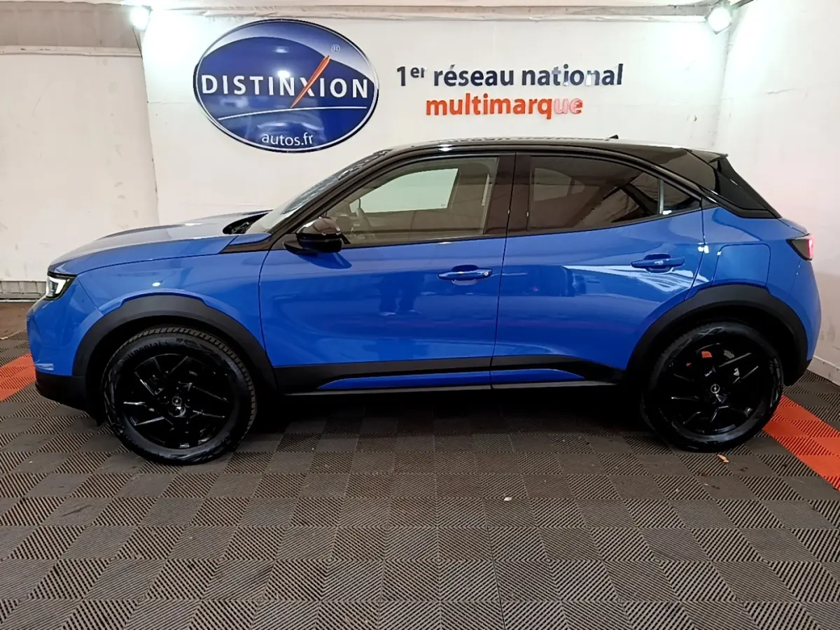 Vue latérale droite d'un Opel Mokka 2024 bleu avec toit noir et jantes noires dans un showroom.