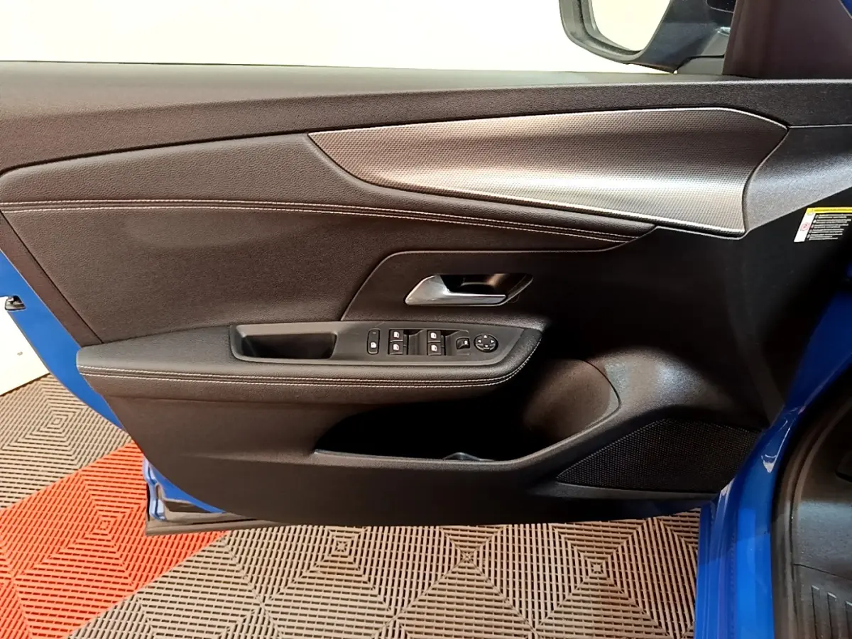 Vue intérieure côté gauche de la porte avant bleue de l’Opel Mokka 2024 avec commandes de vitres et poignée argentée.