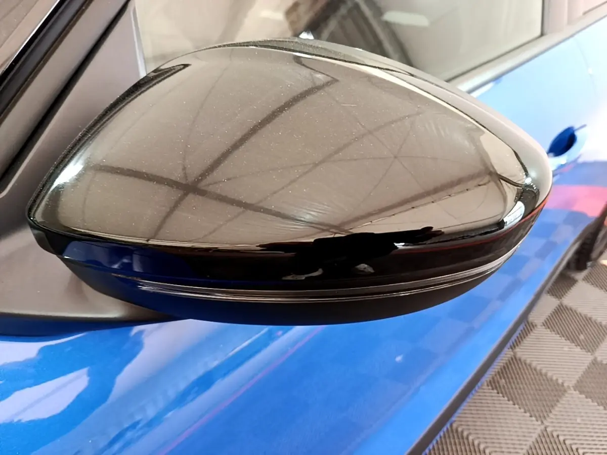 Rétroviseur côté gauche noir brillant sur Opel Mokka bleu, vue rapprochée avec reflet de la structure environnante.