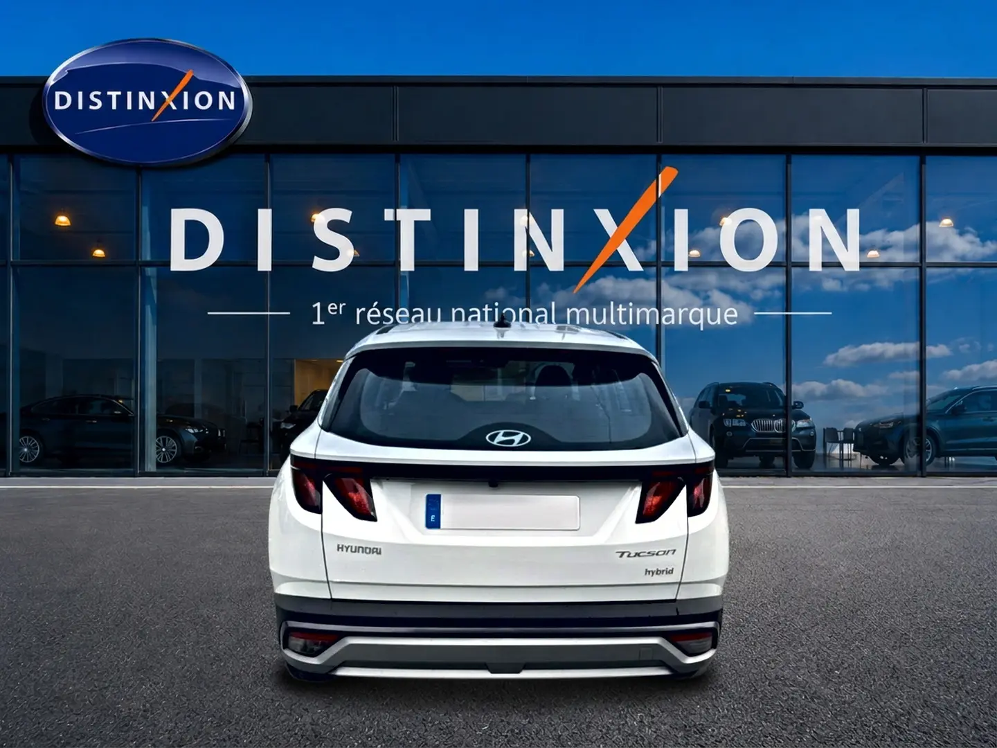 Vue arrière d'un Hyundai Tucson blanc hybride 2026 garé devant une vitrine avec logo Distinxion.