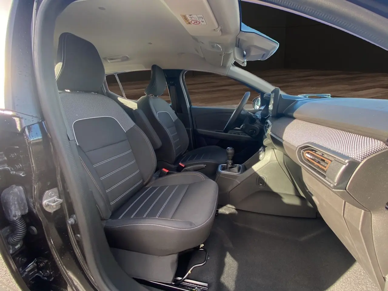 Vue intérieure côté conducteur de la Dacia Sandero Stepway noire 2025, sièges tissu noir et tableau de bord moderne.