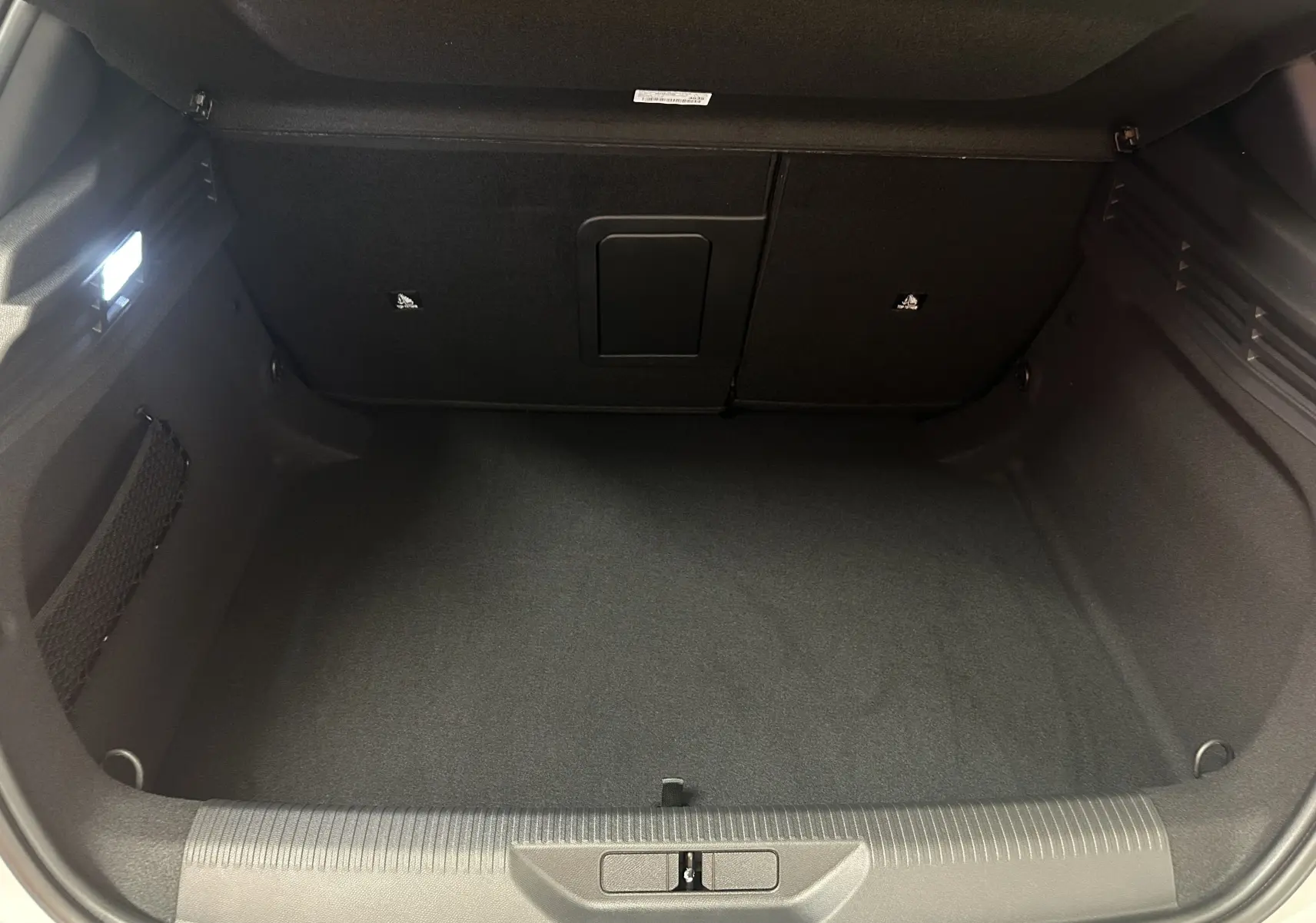 Coffre ouvert de la Peugeot 308 III Ph.2 Hybrid 145 GT blanc Okenite, montrant un espace de chargement propre et éclairé.