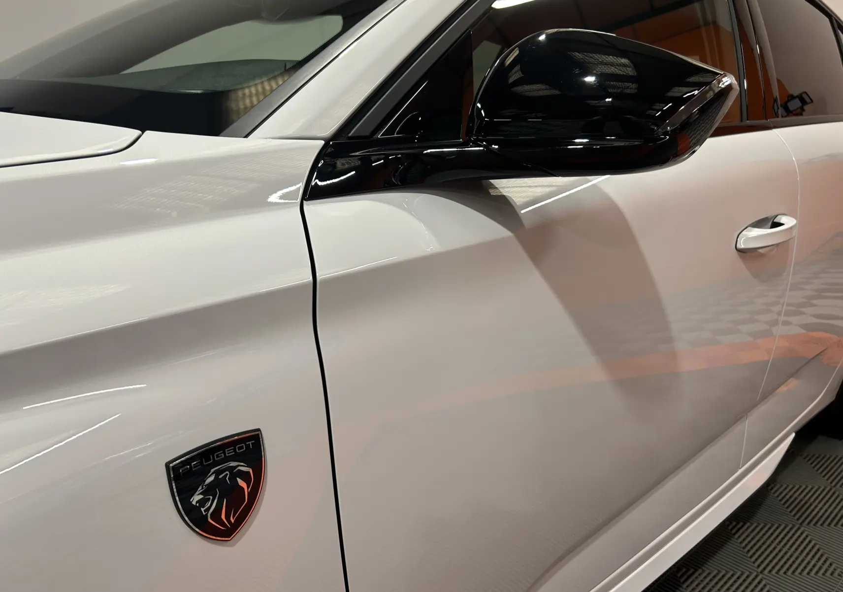 Vue latérale droite rapprochée d'une Peugeot 308 blanche Okenite avec rétroviseur noir brillant et logo lion sur l'aile.