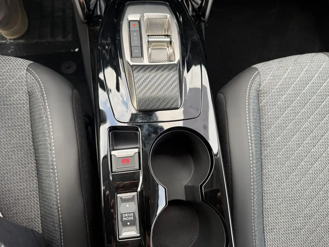 Vue plongeante sur la console centrale noire brillante de la Peugeot 208 Hybrid 145 avec levier de vitesses et porte-gobelets.