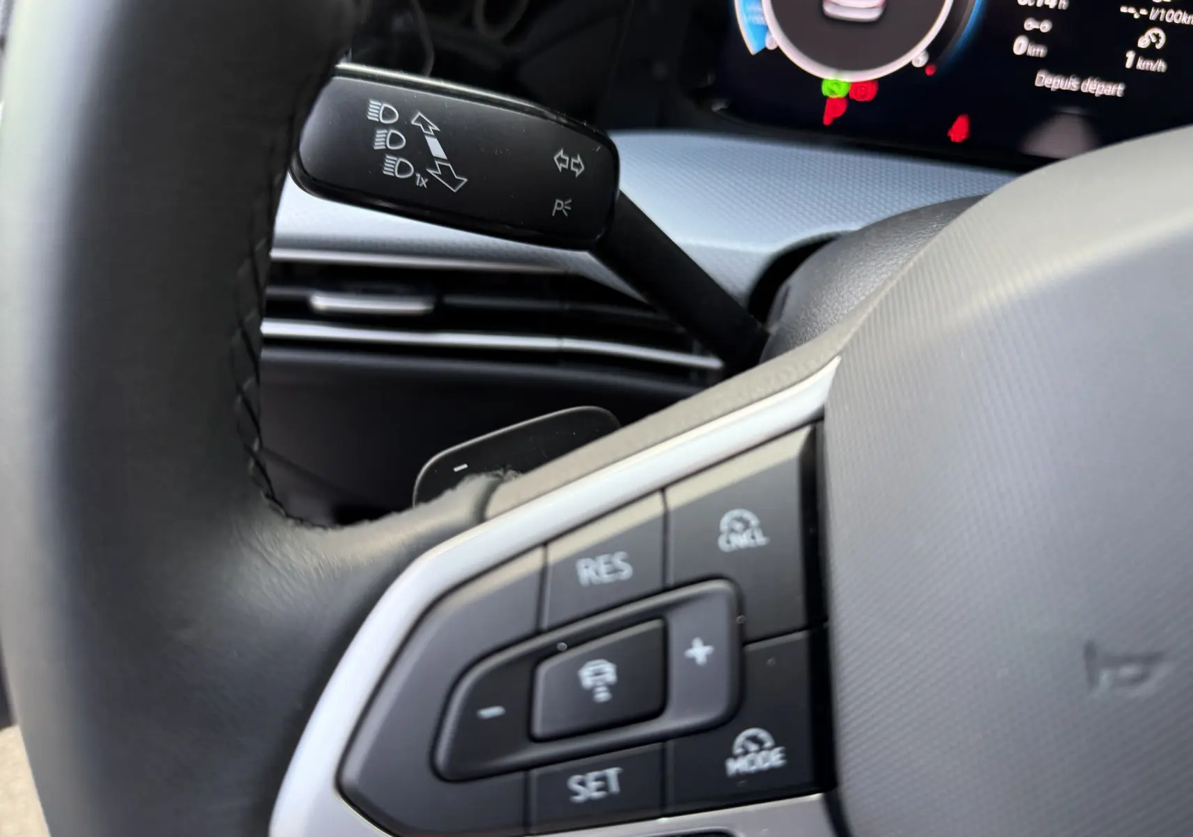 Gros plan sur le volant et commandes du régulateur de vitesse d'une Volkswagen Golf SW gris lunaire, tableau de bord numérique visible.