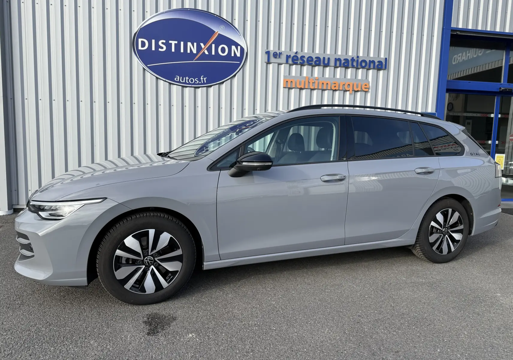Volkswagen Golf SW 2.0 TDI gris lunaire vue 3/4 avant droit, devant un bâtiment avec enseigne Distinxion.