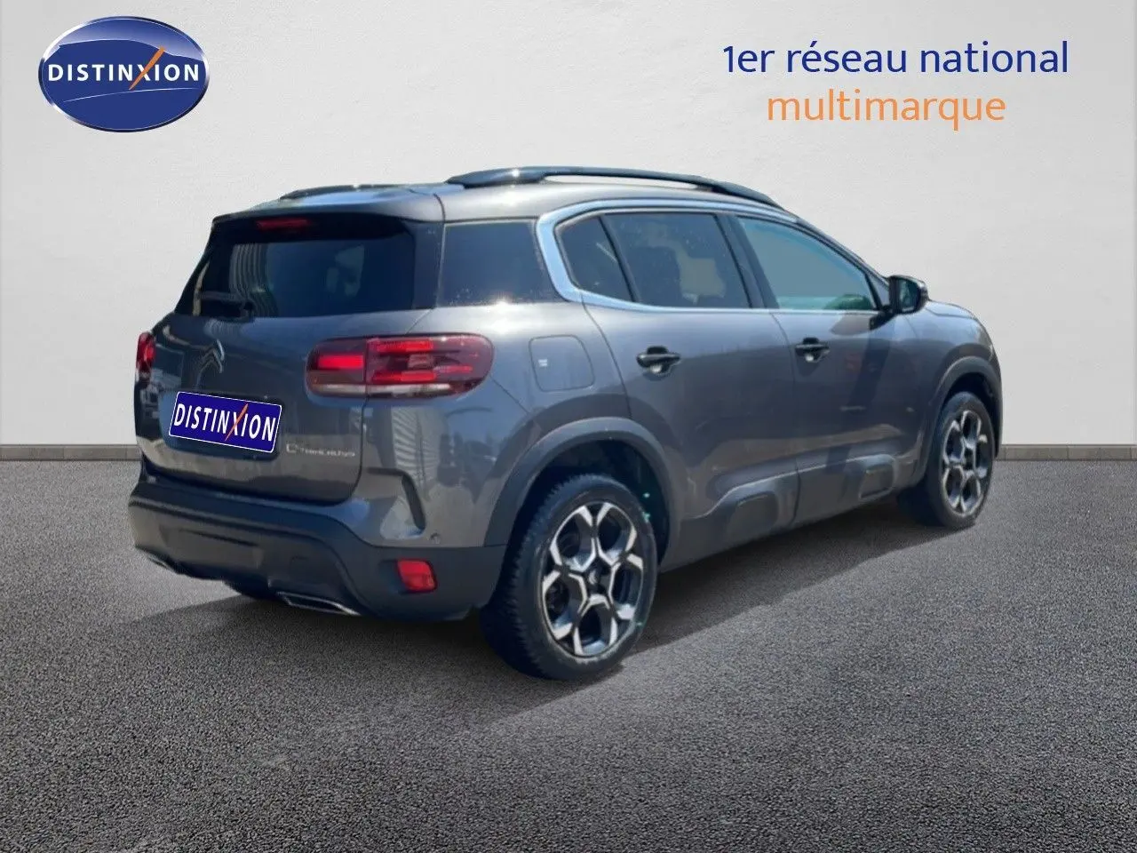 Vue 3/4 arrière droite d'un Citroën C5 Aircross gris platinium métallisé avec jantes bi-ton et barres de toit.