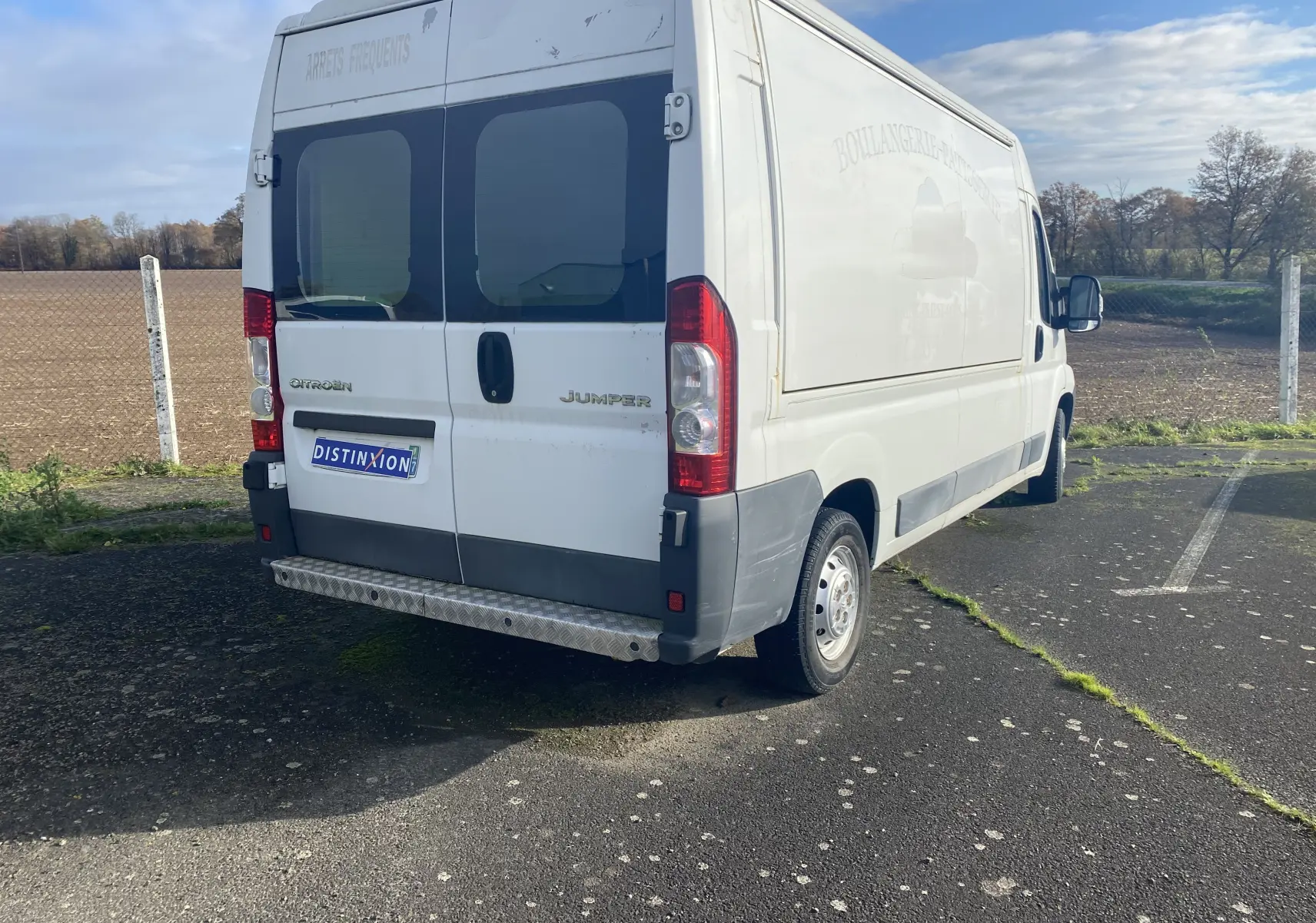 Vue 3/4 arrière droite d'un utilitaire Citroën Jumper blanc avec portes arrière vitrées et marquage publicitaire effacé.