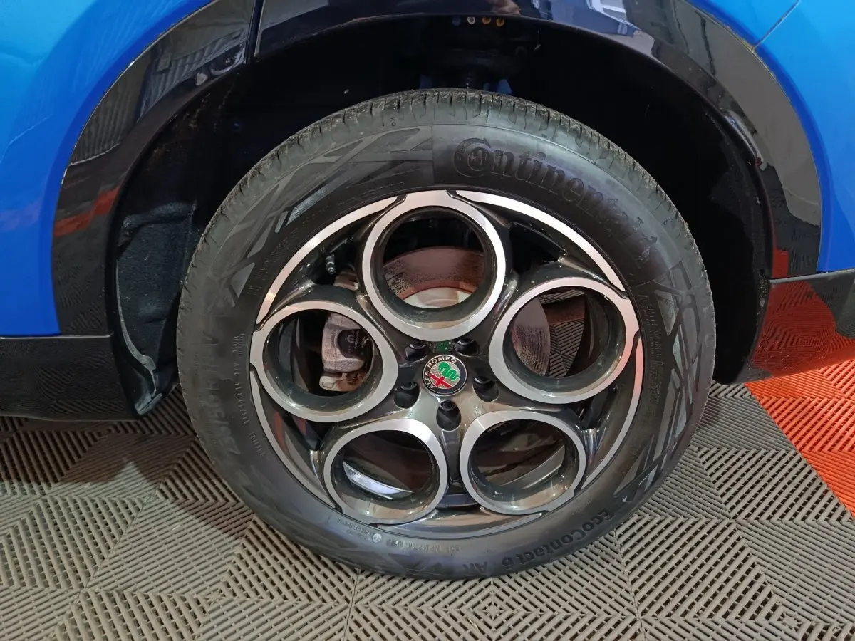 Gros plan sur la roue avant droite d'une Alfa Romeo Tonale bleu, avec jante distinctive à cinq cercles.
